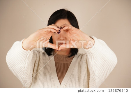 The young woman forms a heart shape with her hands, radiating warmth and affection. Her gentle smile enhances the serene and relaxed pose. A moment filled with love and positivity. 125876340