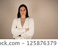 Portrait of sad depressed cute brunette woman folding arms, frowning, wearing white sweater isolated standing on peach background in studio. 125876379