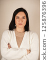 Beautiful young European woman wearing white pullover, folded arms in front of her. 125876396