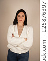Studio portrait of attractive dark-haired smiling woman with arms crossed in front of chest. Isolated background. Vertical photo. 125876397