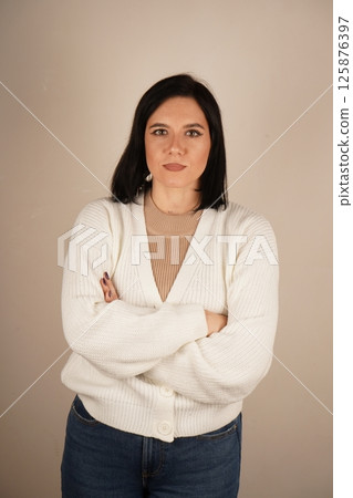 Studio portrait of attractive dark-haired smiling woman with arms crossed in front of chest. Isolated background. Vertical photo. 125876397