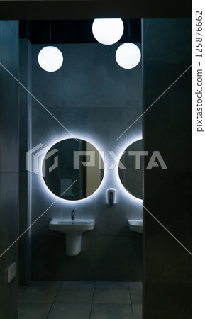 Modern public toilet hall interior with white sinks and round mirror. Nobody inside 125876662