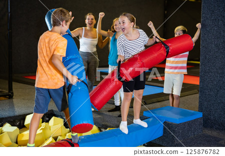 Preteen girl fighting by pugil stick with boy on inflatable beam Preteen girl fighting by pugil stick with boy on inflatable beam 125876782