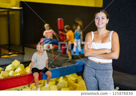 Happy woman in front of children playing in amusement park Happy woman in front of children playing in amusement park 125876830