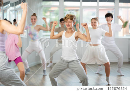 Male boy student repeats movements of unrecognizable teacher during group modern dance class. Male boy student repeats movements of unrecognizable teacher during group modern dance class. 125876834