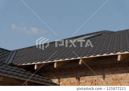 Roof with dark tiles features a skylight, surrounded by brick walls under a clear blue sky, showcasing a modern architectural style 125877221