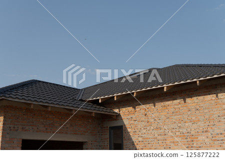 A contemporary home features a black shingled roof with a textured brick facade under a clear blue sky during daylight 125877222