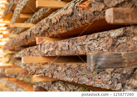 Stacks of logs are arranged orderly, emphasizing their natural bark and wood grain under soft daylight, suggesting timber preparation 125877260