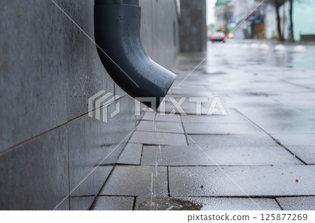 Water continuously drips from a downspout onto the pavement creating small puddles in a city after rain Water continuously drips from a downspout onto the pavement creating small puddles in a city after rain 125877269