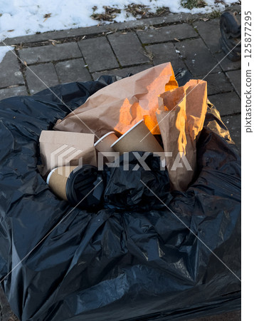A trash bin is overflowing with various discarded food containers, paper wrappers, and bags, highlighting urban waste in wintertime 125877295