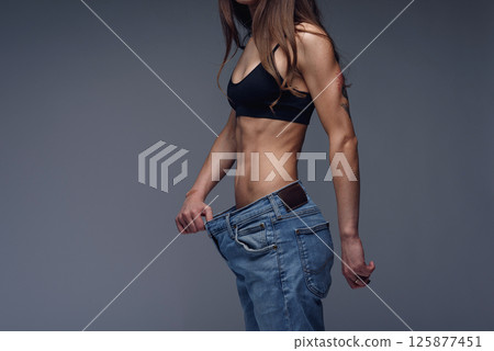 Woman with perfect body demonstrates weight loss, slimming by wearing old big jeans Woman with perfect body demonstrates weight loss, slimming by wearing old big jeans 125877451