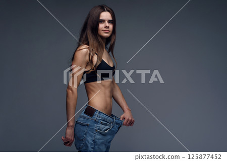 Pretty woman with perfect body demonstrates weight loss, slimming by wearing old big jeans 125877452