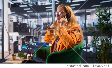 Determined businesswoman speaking on a phone call to ensure project development success, multitasking in a corporate office. Female CEO using remote connection on her smartphone. Camera B. Determined businesswoman speaking on a phone call to ensure project development success, multitasking in a corporate office. Female CEO using remote connection on her smartphone. Camera B. 125877551