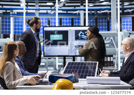 Factory management executives discuss solar panel technology and automation strategies, analyzing data to enhance sustainable manufacturing processes in advanced industrial facility 125877574