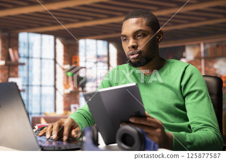Remote worker using laptop and tablet in home office to write emails. Freelancer using digital devices, composing documents in order to deliver finalized project paperwork 125877587