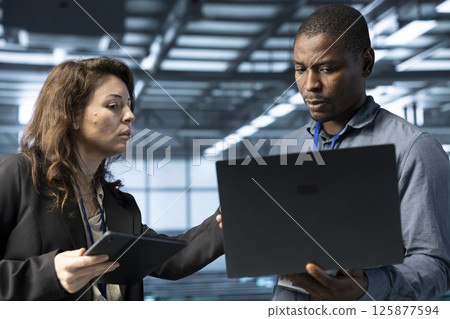 System administrators using laptop in data center, managing server virtualization. IT specialists using notebook in server room, sustaining long term infrastructure reliability System administrators using laptop in data center, managing server virtualization. IT specialists using notebook in server room, sustaining long term infrastructure reliability 125877594
