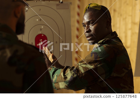 Army general at shooting range training soldiers to learn how to hit targets. Military commander demonstrating how to hit bullseyes, increase gun aiming efficiency during practice 125877648