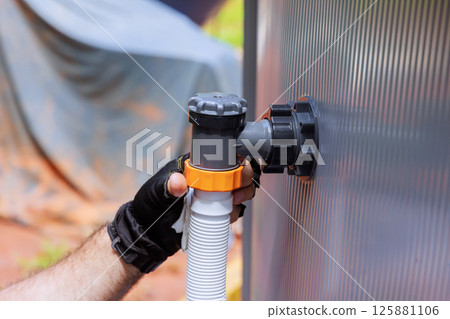 Worker is attaching hose to swimming pump pool system, ensuring secure connections at an outdoor work site 125881106