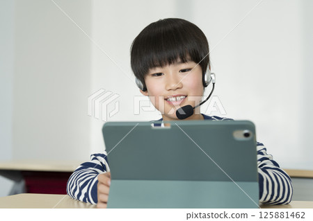 一名四年級男孩戴著耳機，面對著一台平板電腦 125881462