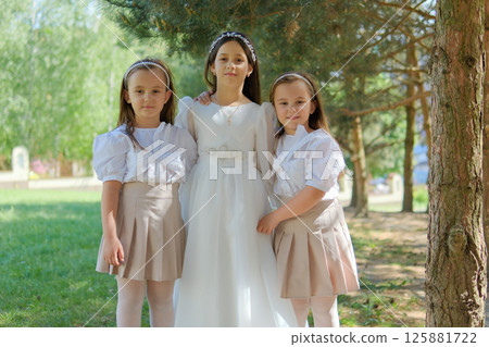 A festive moment is captured in a tender frame with three girls. The girl in an ivory dress looks solemn and harmonious. 125881722