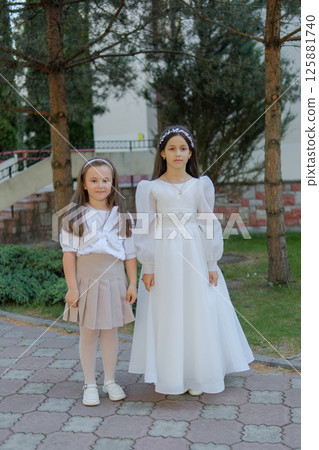 The two sisters are beautifully dressed for the occasion. The child is dressed in a long white dress. 125881740