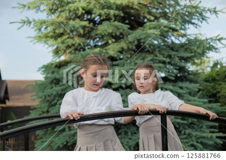 A pair of schoolgirls carefully observe a tiny wonder of nature. Their white clothes make their figures stand out against the dark wood. A pair of schoolgirls carefully observe a tiny wonder of nature. Their white clothes make their figures stand out against the dark wood. 125881766