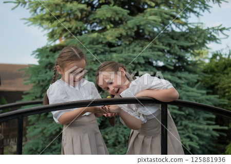 The girls' eyes are fixed on a tiny snail. The braids tied with ribbons complete the image of natural charm. The girls' eyes are fixed on a tiny snail. The braids tied with ribbons complete the image of natural charm. 125881936