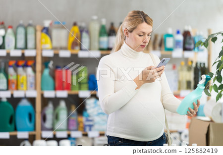 Pregnant woman scanning glass cleaner spray in household store Pregnant woman scanning glass cleaner spray in household store 125882419