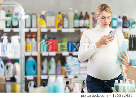 Pregnant woman scanning QR code on shampoo for online payment Pregnant woman scanning QR code on shampoo for online payment 125882425