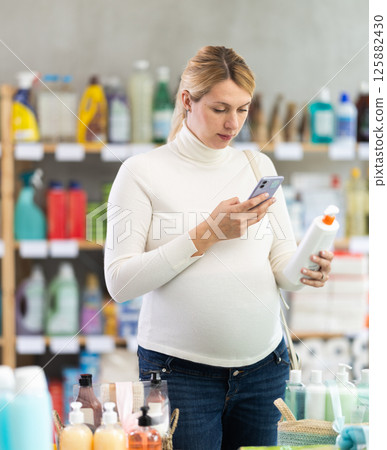 Pregnant shopper scanning barcode on sun lotion with phone Pregnant shopper scanning barcode on sun lotion with phone 125882430
