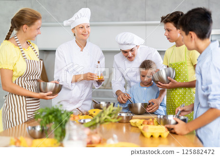Young guy and adult woman cook teaches group of children to cook Young guy and adult woman cook teaches group of children to cook 125882472