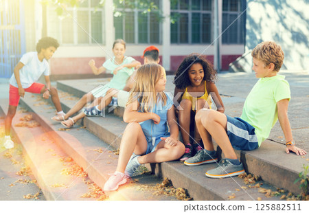 Positive tweenagers friendly blabbing while sitting on steps outdoors 125882511