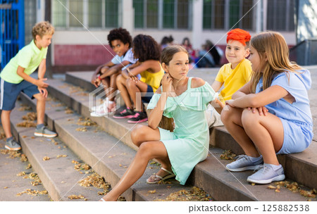 Cheerful preteen girls and boys sitting on steps outdoors and chatting 125882538