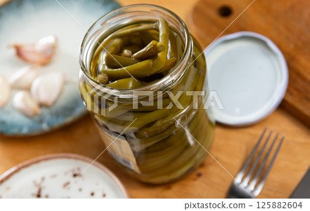There is open jar with pickled green young ramson shoots on table. There is open jar with pickled green young ramson shoots on table. 125882604