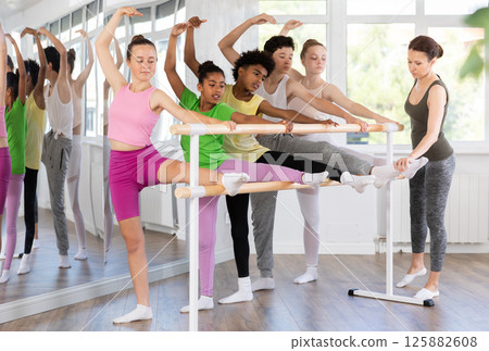 Teenage girl doing leg stretching exercise holding by ballet barre during dance courses 125882608