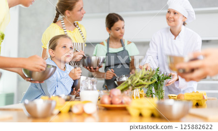 Team of positive teenagers and female chef at cooking classes. Learn to beat raw eggs Team of positive teenagers and female chef at cooking classes. Learn to beat raw eggs 125882622