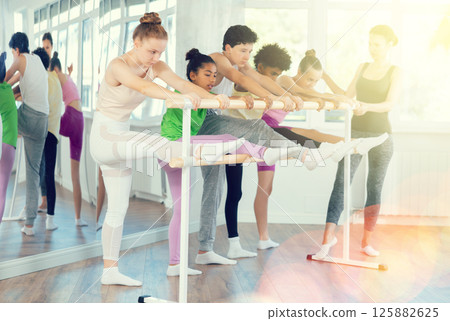 Teenage girl stretching at barre during beginner ballet class Teenage girl stretching at barre during beginner ballet class 125882625