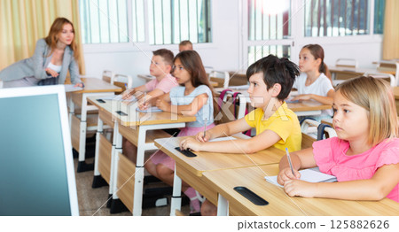 Diligent tweens listening to teacher and writing in notebooks in class 125882626