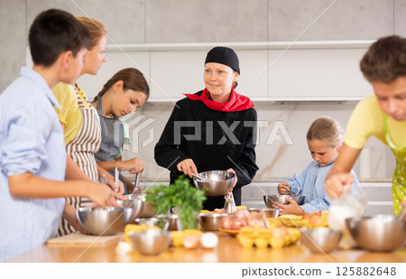 Team of positive teenagers and female chef at cooking classes. Learn to beat raw eggs Team of positive teenagers and female chef at cooking classes. Learn to beat raw eggs 125882648