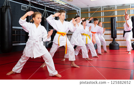 Children wearing karate uniform practicing new moves in group Children wearing karate uniform practicing new moves in group 125882652