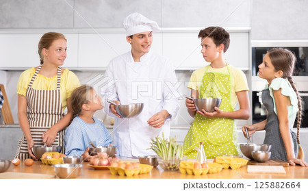 In cooking class, guy cook with bowl in hands tells children participants culinary ticks and tricks 125882664
