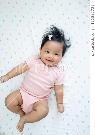 Joyful newborn baby smiling in pink outfit asian infant indoor setting close-up perspective 125882725