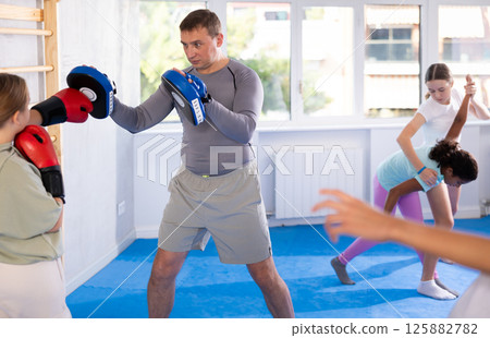 Focused girl hitting the focus mitts held by his boxing trainer in gym Focused girl hitting the focus mitts held by his boxing trainer in gym 125882782