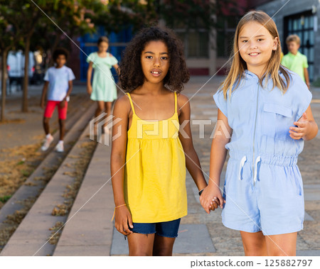 Two cheerful preteen girls enjoying walk along city street Two cheerful preteen girls enjoying walk along city street 125882797