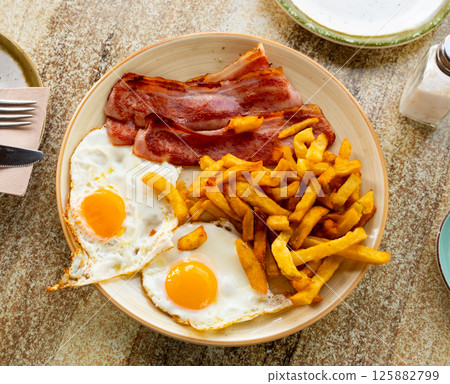 Fried eggs with sliced bacon and french fries 125882799