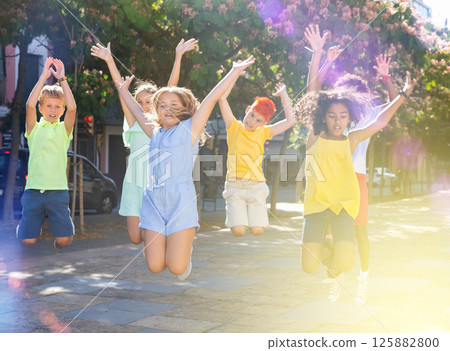Cheerful preteen friends jumping on summer city street Cheerful preteen friends jumping on summer city street 125882800