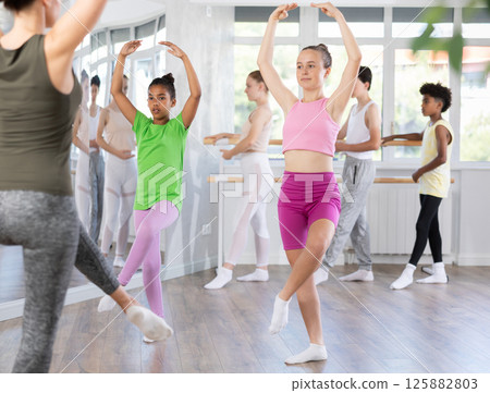 Positive teenage girl practicing ballet positions standing in row with others 125882803