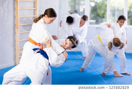 Karate training - girl and boy of different nationalities in pairs exercising karate movements during group training in gym 125882829