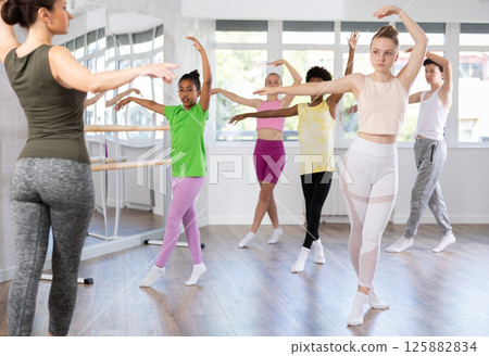 Slender teen girl doing fourth position of ballet in group during choreography classes Slender teen girl doing fourth position of ballet in group during choreography classes 125882834