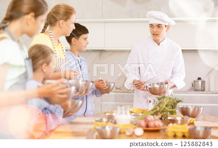 Friendly young chef running culinary courses for group of children 125882843